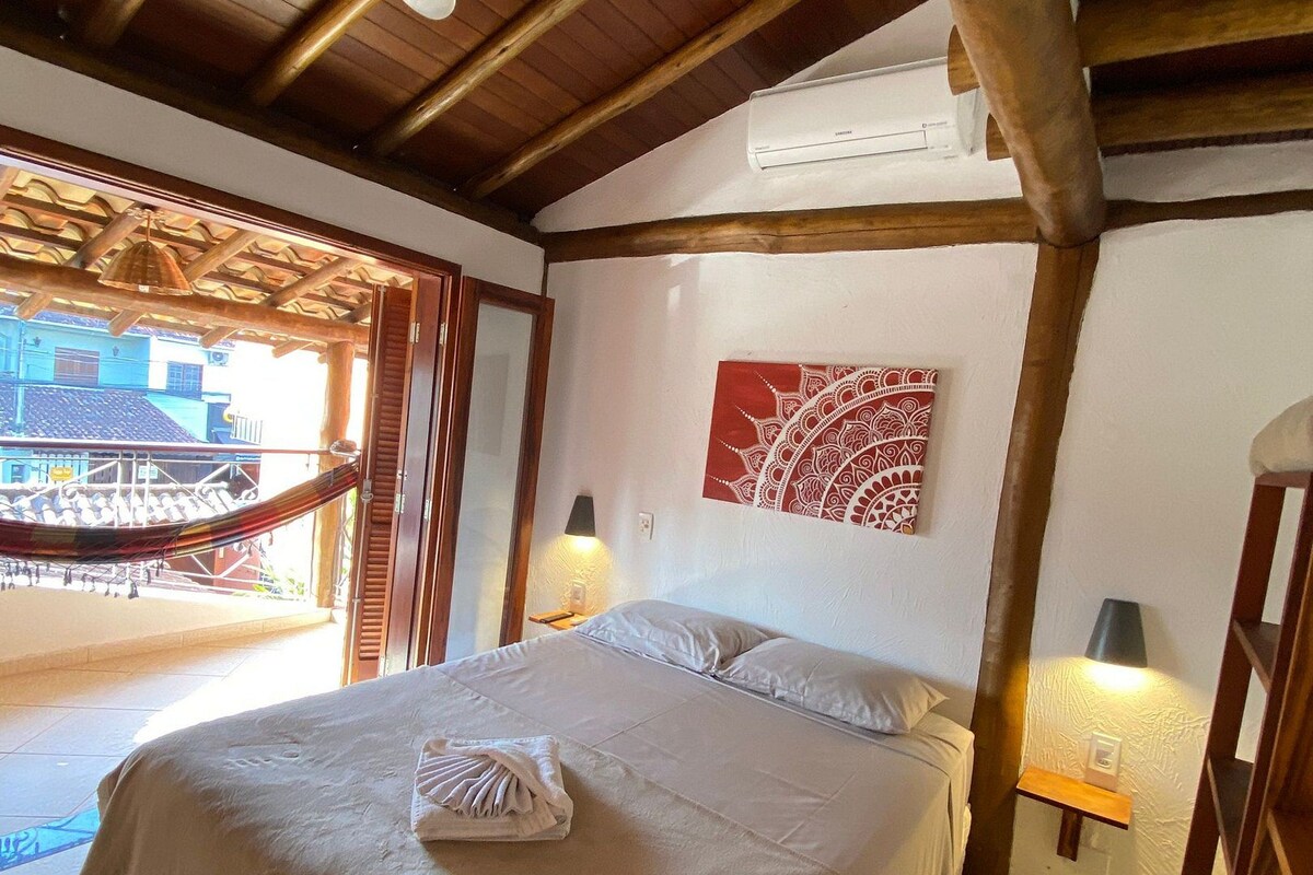 A bedroom with a bed, a ceiling fan, a hammock outside, and a view of buildings.