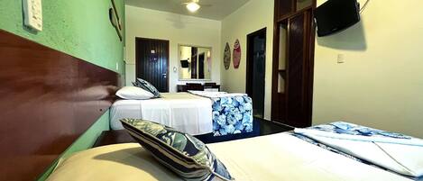 A hotel room with two beds, a television mounted on the wall, and a door leading to another room.