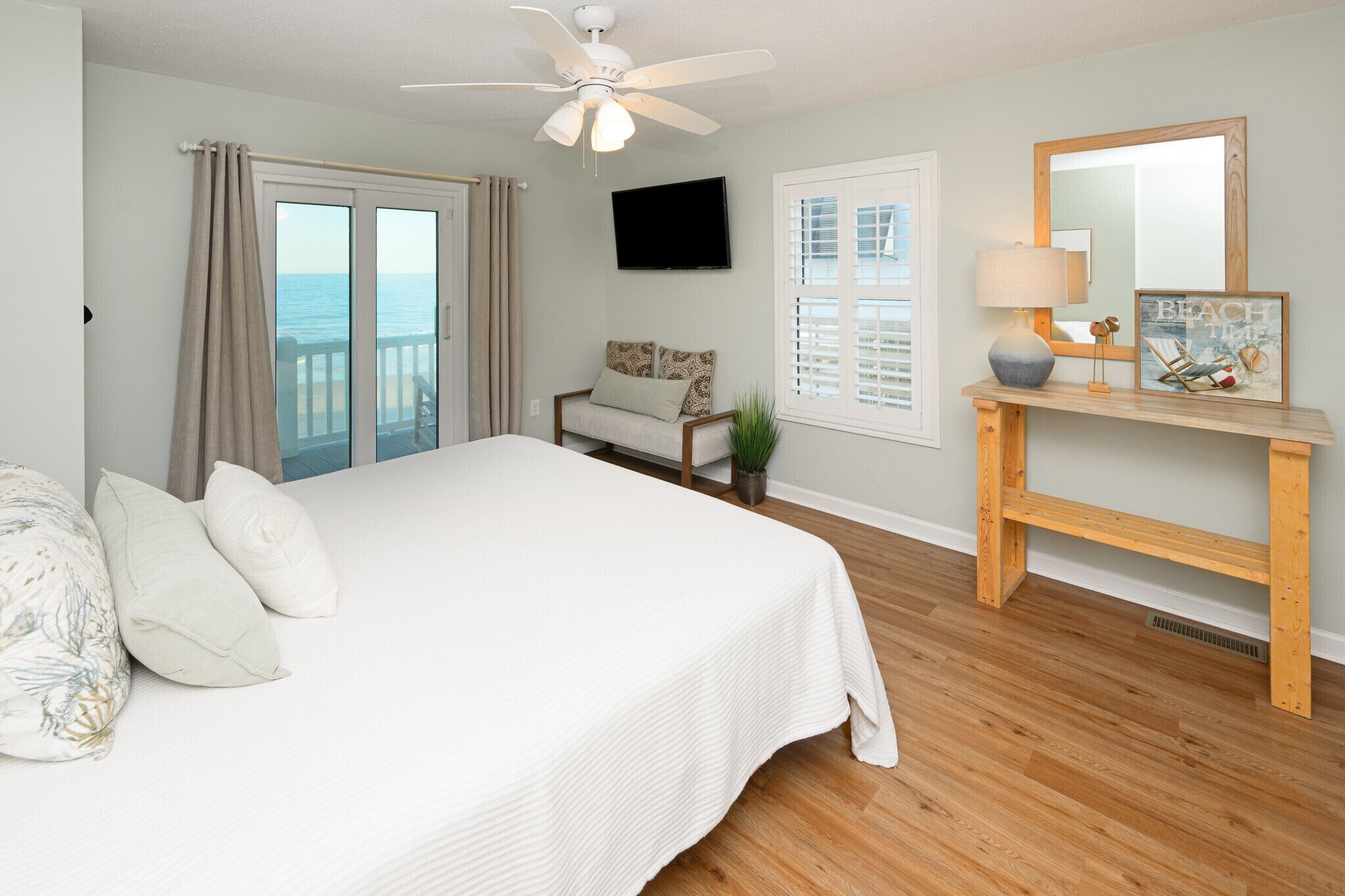 A bedroom with a bed, a ceiling fan, a TV, a bench, and a window with shutters.