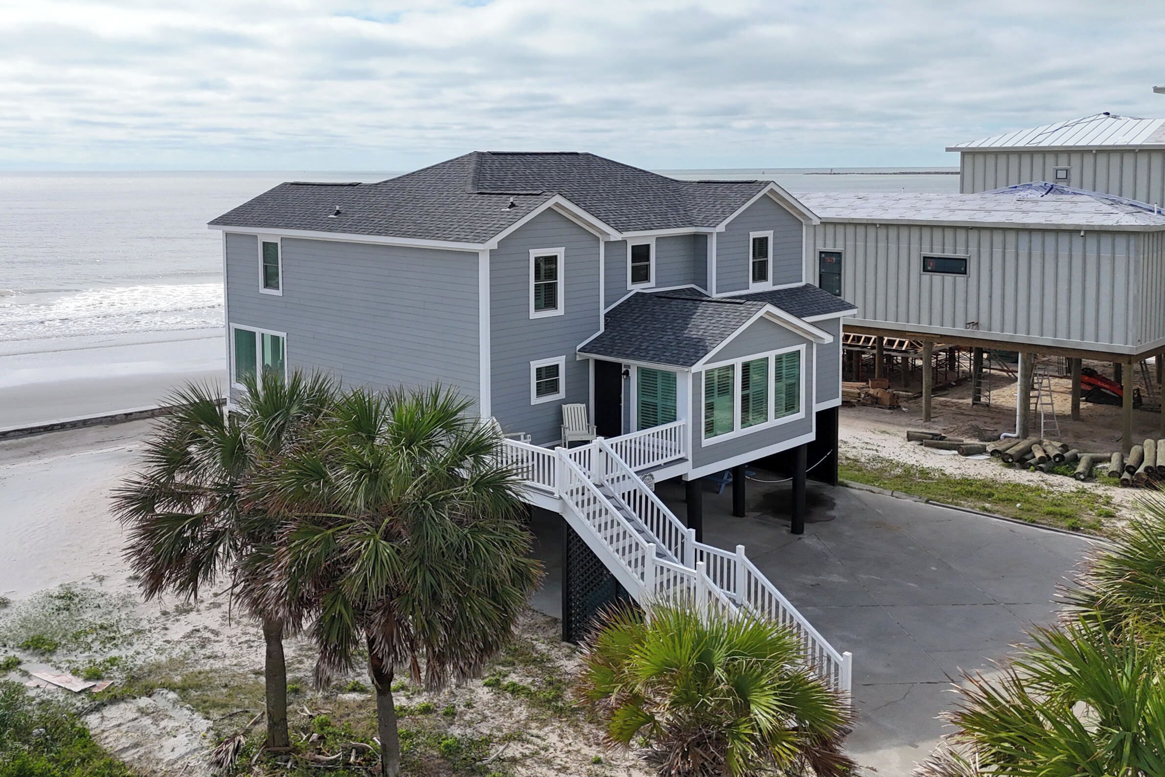 A coastal house with a balcony, a staircase, and a view of the beach.