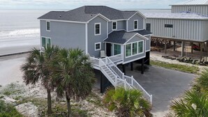 A coastal house with a balcony, a staircase, and a view of the beach.