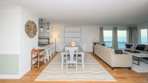 A spacious living area with a dining table, sofa, and large windows overlooking the sea.