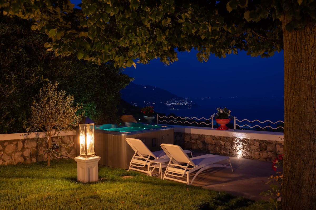 Un área de hidromasaje al aire libre con sillones de descanso, una pared de piedra y vista al mar de noche.