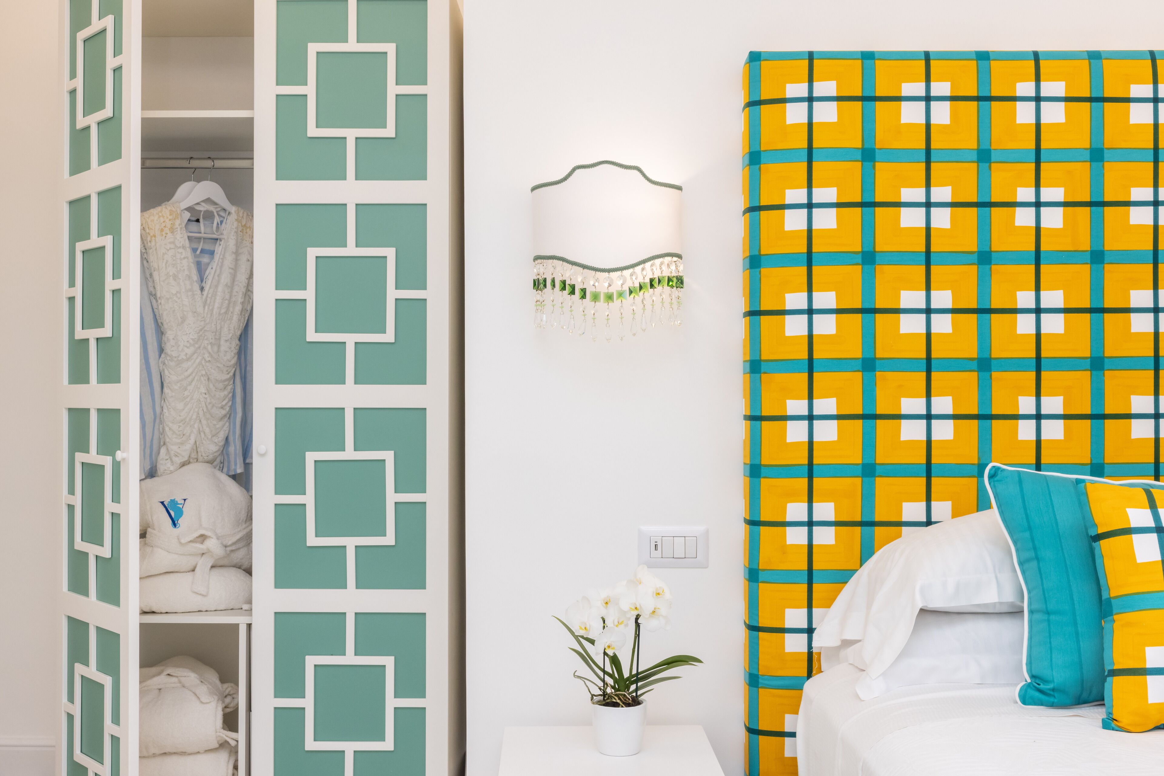 A bedroom with a bed, a nightstand, a wall-mounted lamp, and a closet with hanging clothes.
