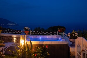 Un bain à remous doté d’un mur en pierre et agrémenté de plantes en pot, offrant une vue sur la côte.