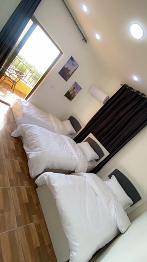 A hotel room with a large bed, a small table, and a chair. There is a window with curtains, and a wall-mounted air conditioner. - Lacasa chalet panoramic view to dead sea (Sweimeh)