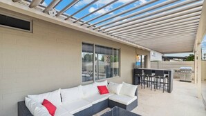 Um pátio externo com um sofá modular, uma churrasqueira e uma área de refeições.