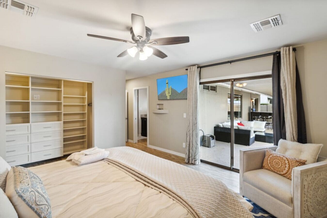 A bedroom with a bed, a chair, a wardrobe, and a sliding glass door leading to a bathroom.
