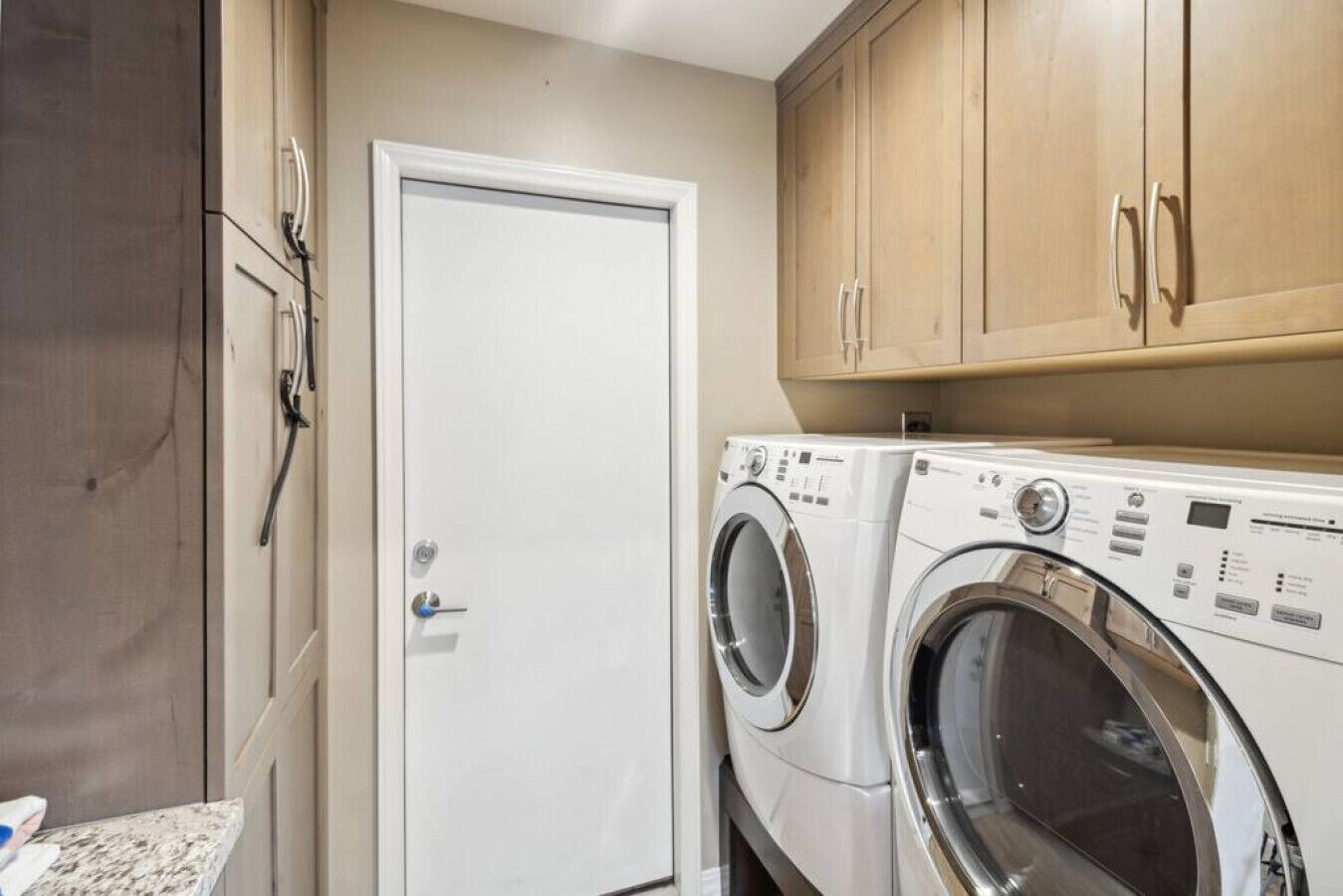 A laundry room with a white door, wooden cabinets, and a front-loading washing machine.