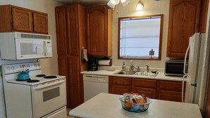 A compact kitchen with wooden cabinets, a white stove, a microwave, a dishwasher, and a small window above the sink. - Cozy Home on Lake Brownwood  (Brownwood)