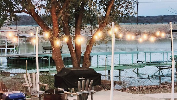 An outdoor patio area with a grill, chairs, and string lights. - Cozy Home on Lake Brownwood  (Brownwood)