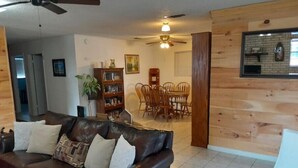 A living room with a leather sofa, wooden walls, a dining area with chairs, and a ceiling fan. - Cozy Home on Lake Brownwood  (Brownwood)
