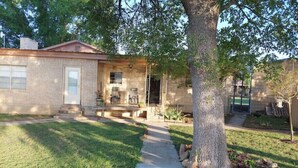 A single-story house with a brick exterior, a front porch with a bench, and a large tree in the yard. - Cozy Home on Lake Brownwood  (Brownwood)