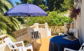 An outdoor patio area with a blue umbrella, white chairs, and a round table with a blue tablecloth. - Comfortable | Very quiet area | 2km from Cala Cap Blanc - Punta Estrella (VC)
