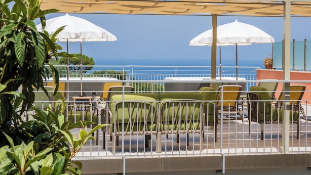 A terrace with outdoor seating, white umbrellas, and a view of the ocean.