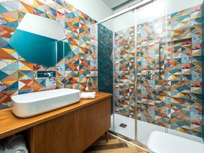A bathroom with a white sink, wooden vanity, and a glass shower enclosure.