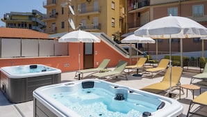 A rooftop pool area with hot tubs, lounge chairs, and umbrellas.