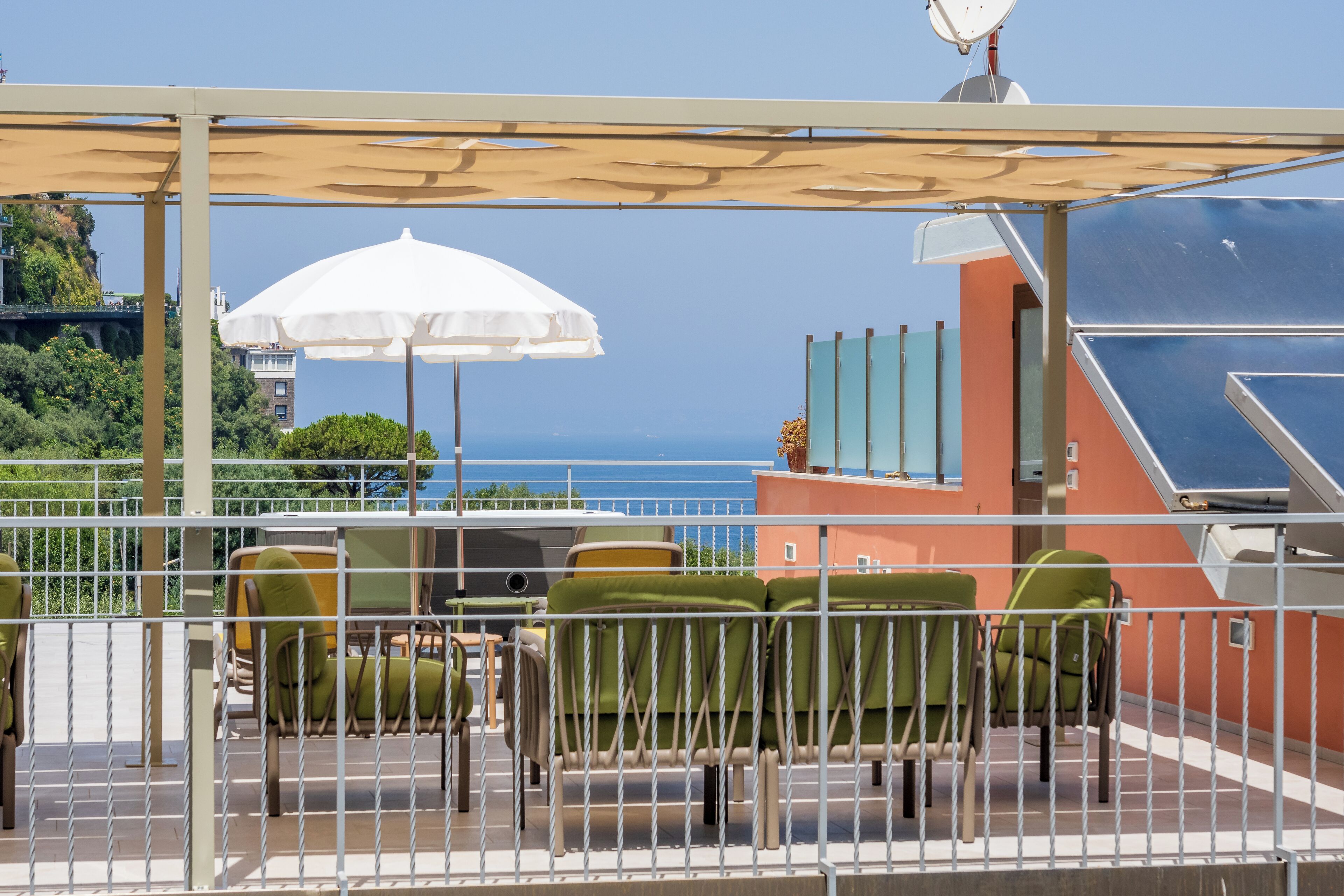 A terrace with outdoor seating, a white umbrella, and a view of the sea.