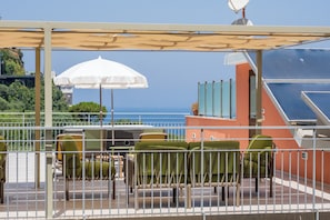 A terrace with outdoor seating, a white umbrella, and a view of the sea.