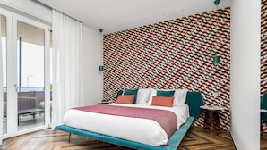A modern bedroom with a large bed, a patterned wall, and a sliding glass door to a balcony.