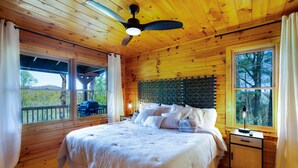 A wooden cabin bedroom with a large bed, a nightstand, and a ceiling fan. - 🌿 Summer Retreat  *  HotTub  *  Mountain Views  *  2 Masters  *  Pets OK (Ellijay)
