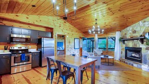 A spacious kitchen with modern appliances, a dining area with a large table, and a stone fireplace. - 🌿 Summer Retreat  *  HotTub  *  Mountain Views  *  2 Masters  *  Pets OK (Ellijay)