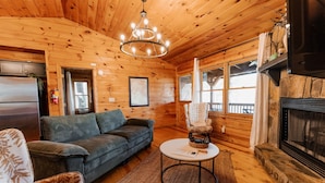 A cozy cabin interior with a wooden ceiling, a fireplace, a sofa, a chair, and a small table. - 🌿 Summer Retreat  *  HotTub  *  Mountain Views  *  2 Masters  *  Pets OK (Ellijay)