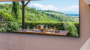 A dining table set with glasses and a pitcher, overlooking a lush green landscape with hills and a clear sky. - Templari by Interhome (Santa Luce)