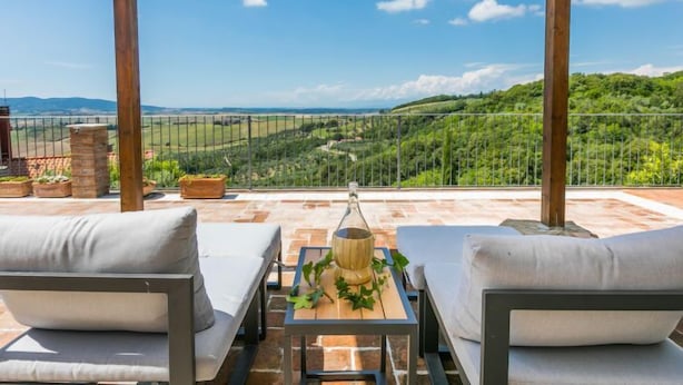 A covered outdoor seating area with two cushioned chairs and a table, overlooking a scenic landscape with hills and a clear sky. - Templari by Interhome (Santa Luce)