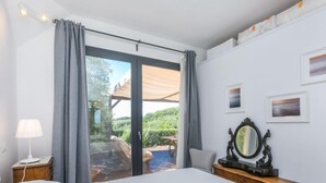 A bedroom with a large bed, a nightstand, a lamp, a dresser with a mirror, and a view of the outdoors through a sliding glass door. - Templari by Interhome (Santa Luce)