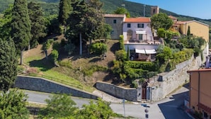 A hillside property with a stone retaining wall, a paved road, and a mix of residential buildings with red-tiled roofs. - Templari by Interhome (Santa Luce)