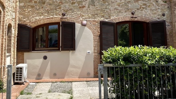 A stone building with a sloped roof, a small courtyard with a metal fence, and a clear blue sky. - Tripyou by Interhome (Guardistallo)