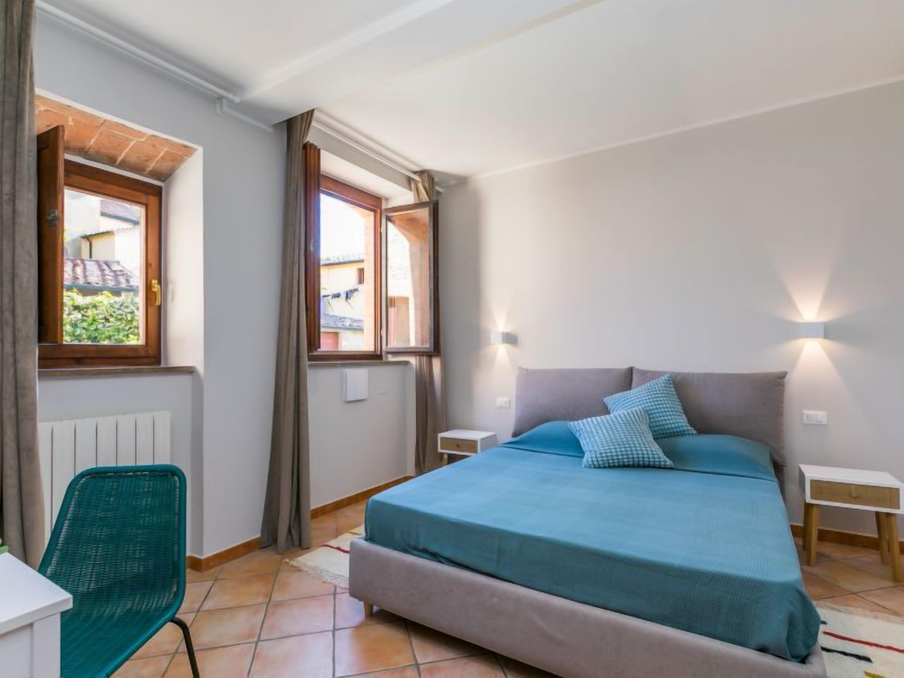 Une chambre à coucher avec un lit, une chaise, une table de chevet et une fenêtre avec des rideaux.