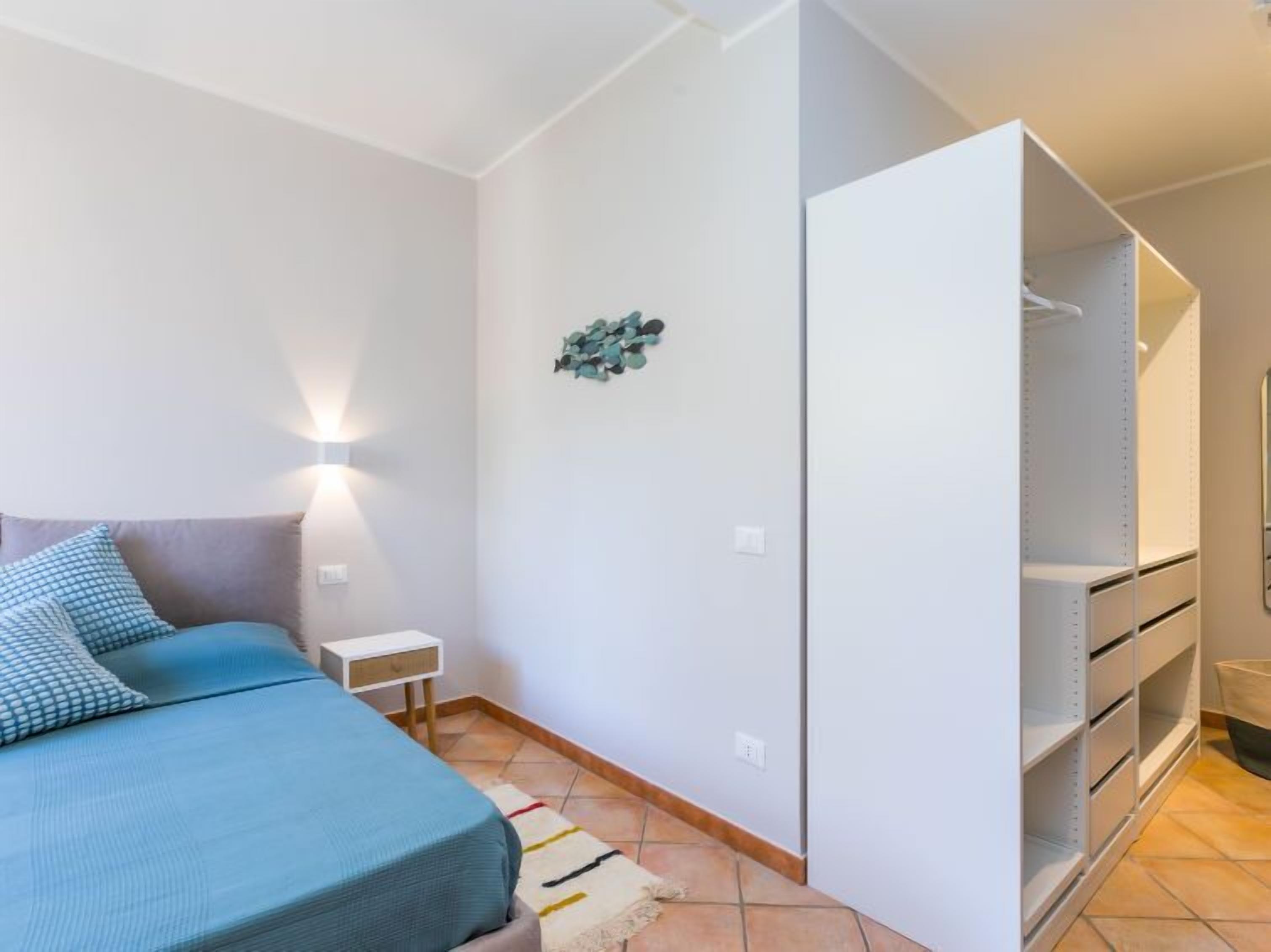 Une chambre à coucher comprenant un lit, une table de chevet, une lampe fixée au mur, une armoire avec des étagères et un élément décoratif mural.