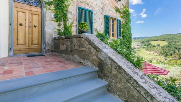 Un edificio in pietra con una porta di legno e persiane verdi, una scala in pietra e vista su una valle.
