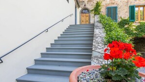 Una scala conduce a un edificio in pietra con una porta in legno e persiane verdi.