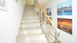 Un escalier doté d’une rampe métallique et d’une main courante en bois, menant à un palier où se trouve un pot de fleurs.