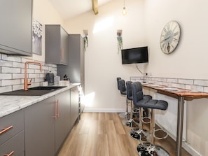 Una cocina moderna con gabinetes grises, un grifo de cobre, un televisor negro montado en la pared y una mesa de comedor de madera con taburetes de bar.