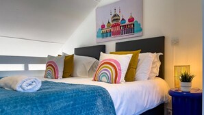 A neatly made bed with a blue quilt, white bedding, and colorful pillows. A painting of a mosque is on the wall above the bed. - On the Water 4 With Free Parking By My Getaways (Brighton)