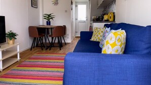 A living room with a blue sofa, colorful rug, and a dining area with a table and chairs. - On the Water 4 With Free Parking By My Getaways (Brighton)