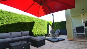 An outdoor patio with a red umbrella, a sofa, two chairs, and a small table. - Villa Mallorca by Interhome (Miami Platja)