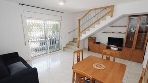 A living room with a sofa, a dining table with chairs, a staircase, a TV, and a cabinet. - Villa Mallorca by Interhome (Miami Platja)