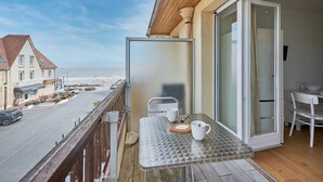 A balcony with a table, chairs, and a view of the street and ocean. - Un Balcon sur la Mer - Appt à 30m de la plage (Saint-Aubin-sur-Mer)