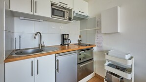 A modern kitchen with white cabinets, stainless steel appliances, a wooden countertop, and a built-in oven. - Un Balcon sur la Mer - Appt à 30m de la plage (Saint-Aubin-sur-Mer)
