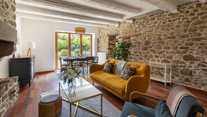 A cozy living room with a stone wall, a yellow sofa, and a dining area with a view of greenery.