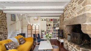 A cozy living room with a yellow sofa, a white coffee table, a bookshelf, and a stone fireplace.
