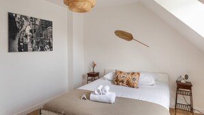 Une chambre d’hôtel bien aménagée, avec un grand lit, un luminaire suspendu, une décoration en plumes fixée au mur et une photographie en noir et blanc encadrée.