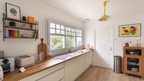 Une cuisine moderne avec des armoires blanches, un plan de travail en bois, une grande fenêtre et un luminaire suspendu jaune.