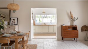 Une cuisine moderne avec des meubles blancs, une table à manger en bois et un luminaire suspendu.