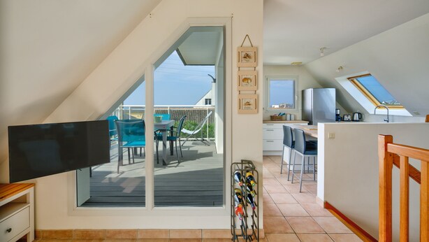Una cocina amplia con una isla grande, un comedor con sillas azules y un puerta corrediza de vidrio que da a una terraza.